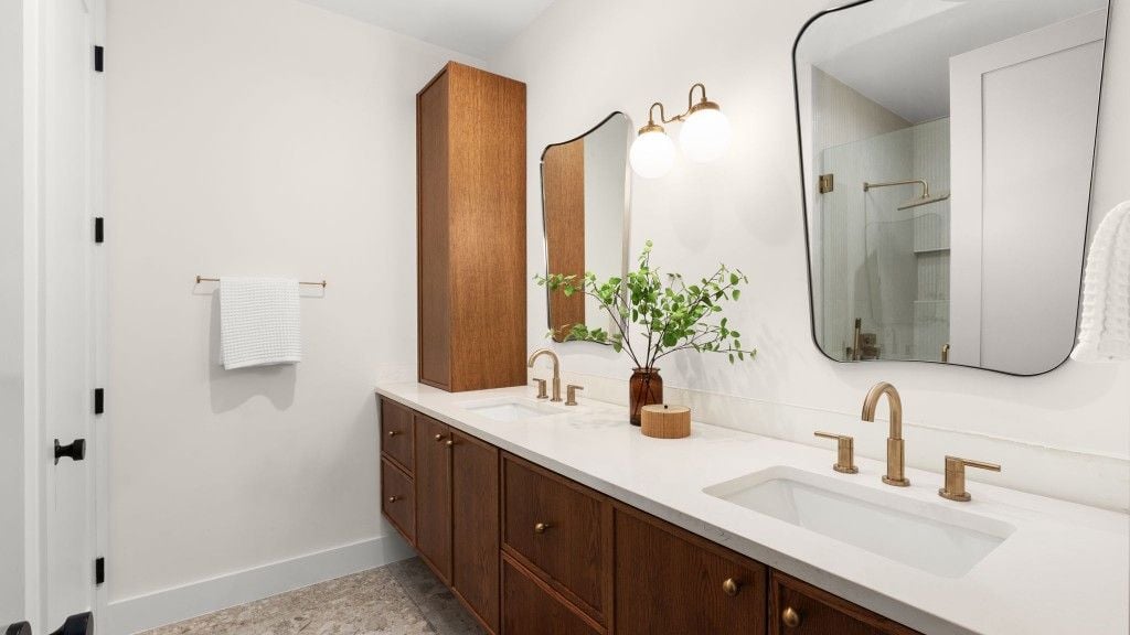 Primary bathroom double vanity in warm wood with brass fixtures