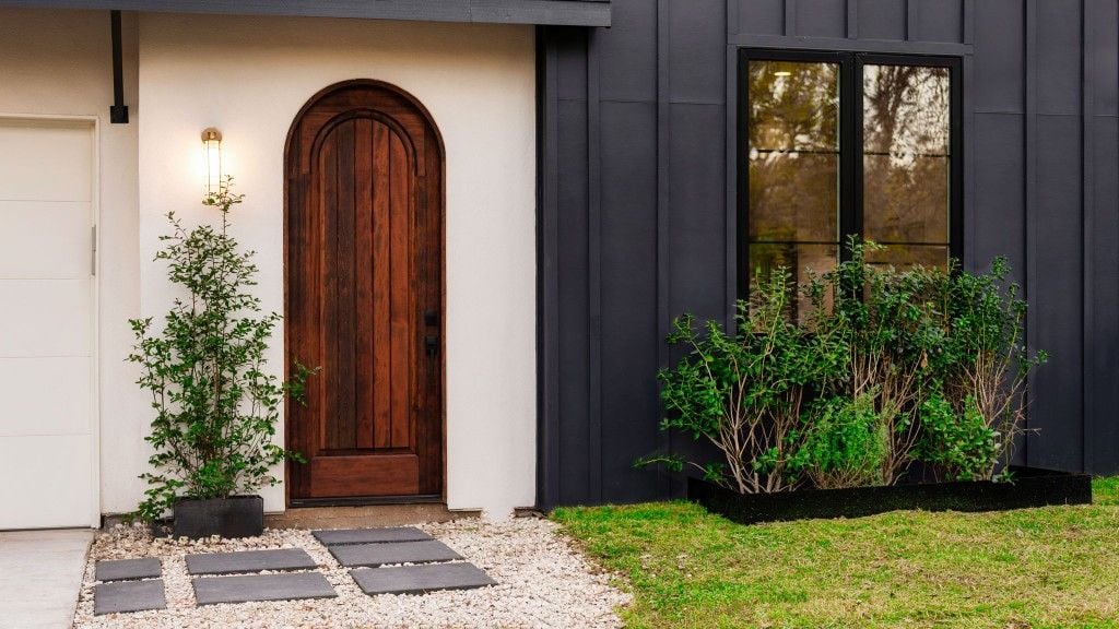 Arched wood front door with white stucco and charcoal vertical siding at Majestic Enclave