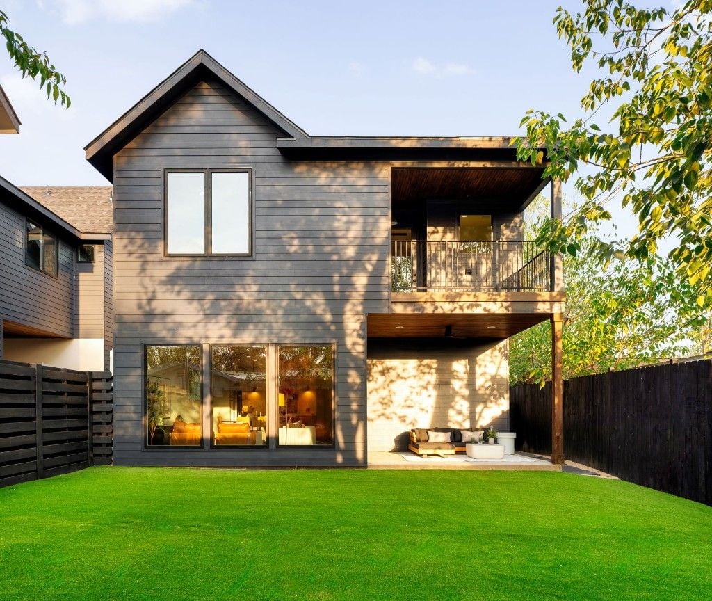 Rear exterior with dark siding, covered patio, balcony, and turf lawn at Majestic Enclave